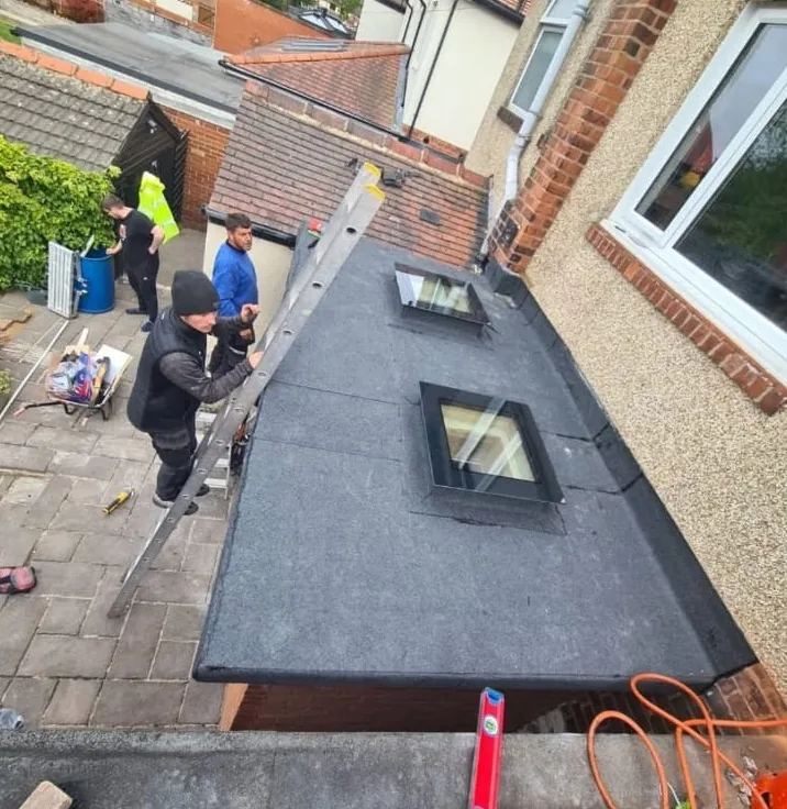 Roofers finishing a felt flat roof with two roof lights on an extension